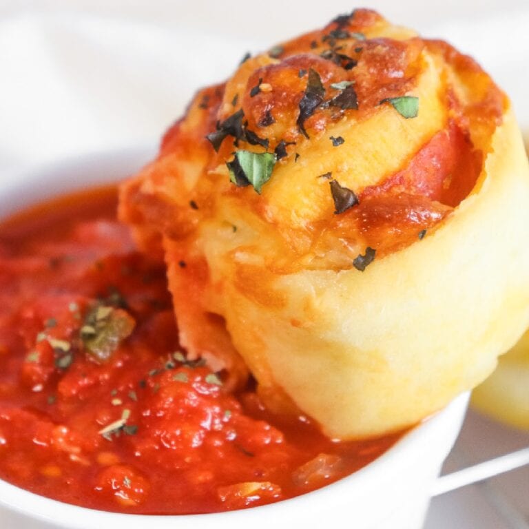 Homemade pepperoni pinwheel being dipped into marinara sauce.