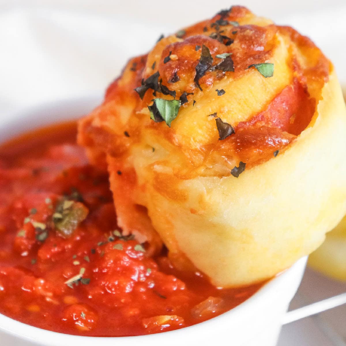 Homemade pepperoni pinwheel being dipped into marinara sauce.