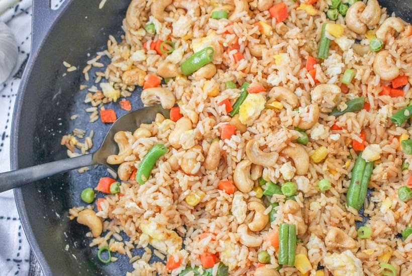 Cashew nut fried rice in a black skillet with a serving spoon.