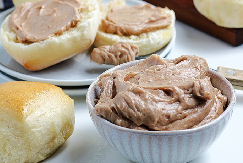 A small ramekin bowl of homemade Texas roadhouse cinnamon honey butter with yeast rolls in the background.