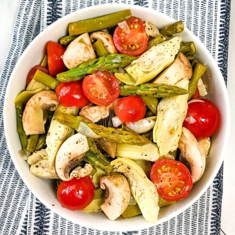 Overhead view of easy vegetable salad with tomatoes, asparagus, artichokes and mushrooms in a white bowl.