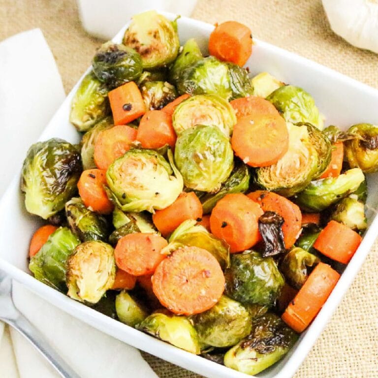 Roasted Brussels sprouts and carrots in a white serving bowl next to a fork.