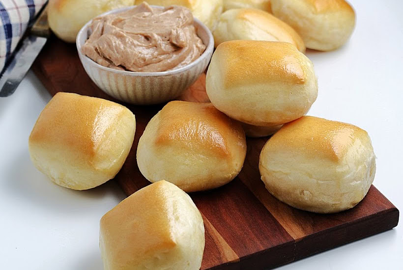 A batch of copycat Texas Roadhouse rolls made from scratch on a cutting board with a bowl of signature butter. 