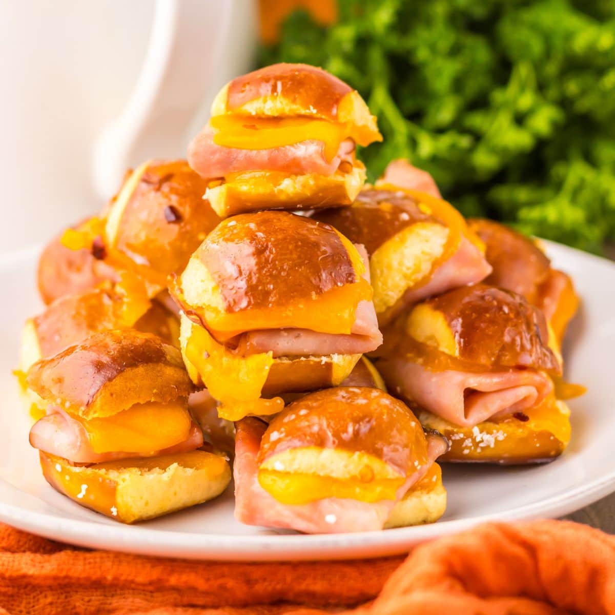 Mini ham and cheese pretzel bites stacked on a white plate.