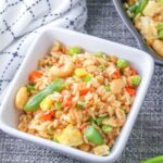 Square white bowl filled with cashew fried rice on a gray placemat.