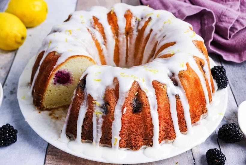 Blackberry bundt cake with lemon drizzle on a white serving platter.