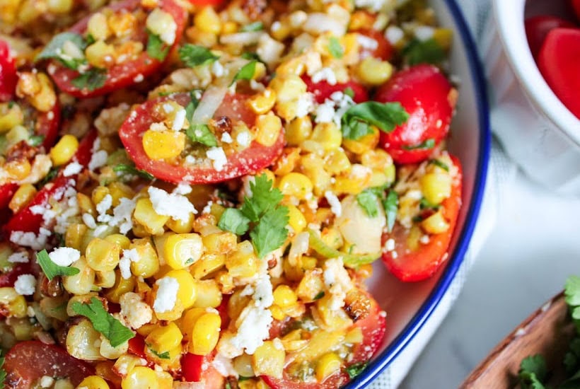 Close up of a bowl of roasted corn salad with fresh cilantro, tomato, and queso fresco cheese in a bowl.