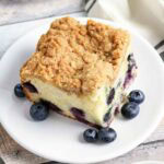 Closeup view of a slice of blueberry sour cream coffee cake and fresh berries on a white round plate.