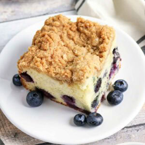 Closeup view of a slice of blueberry sour cream coffee cake and fresh berries on a white round plate.