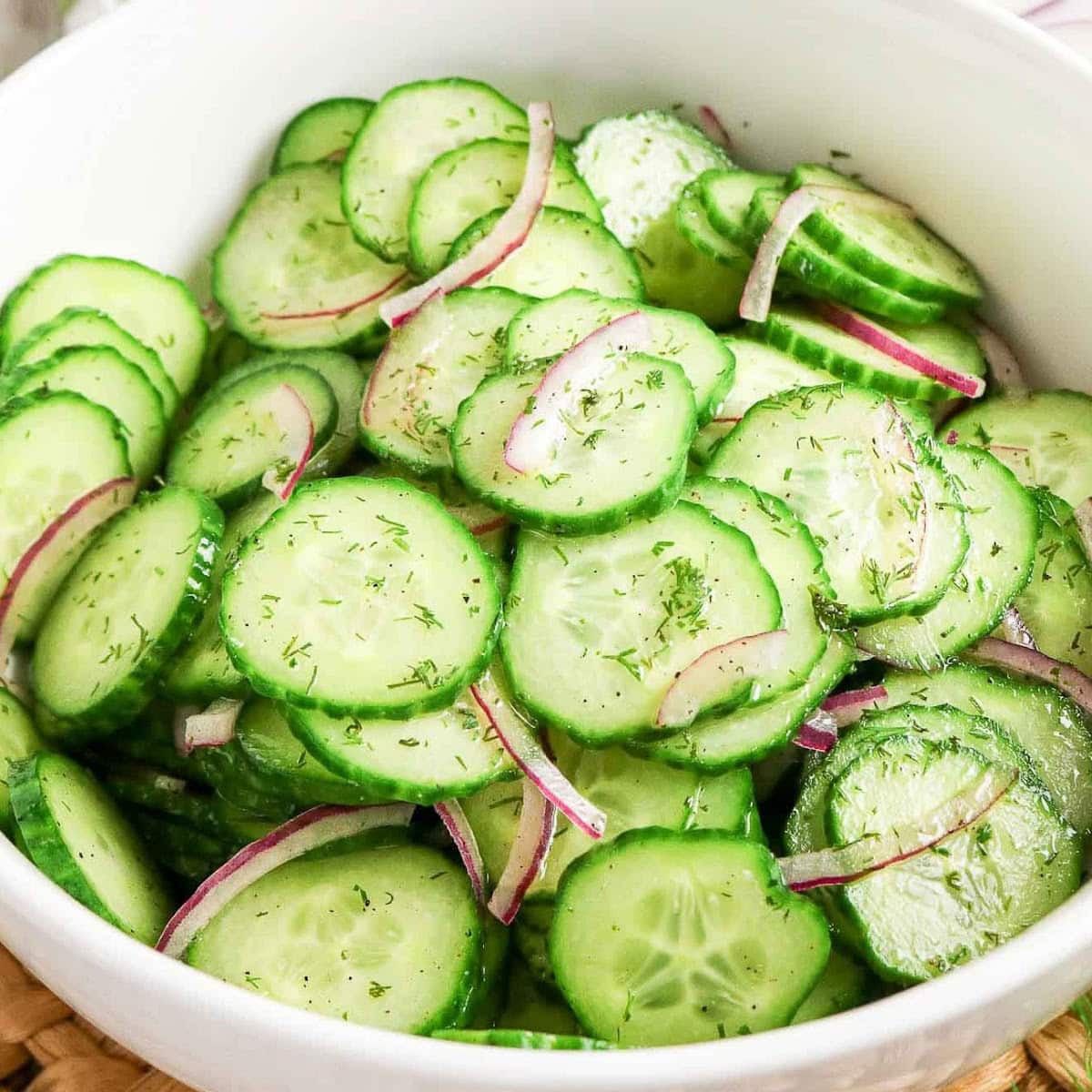 Close up view of Cucumber Dill Salad with red onion in a white bowl.