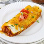 A serving of Frozen Breakfast Burrito Casserole garnished with chopped tomatoes and cilantro on a white plate.