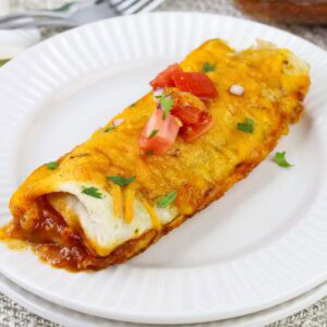 A serving of Frozen Breakfast Burrito Casserole garnished with chopped tomatoes and cilantro on a white plate.
