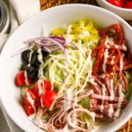 Closeup view of a white bowl filled with Italian Grinder Salad with deli meats, cheese, veggies and a creamy homemade dressing.