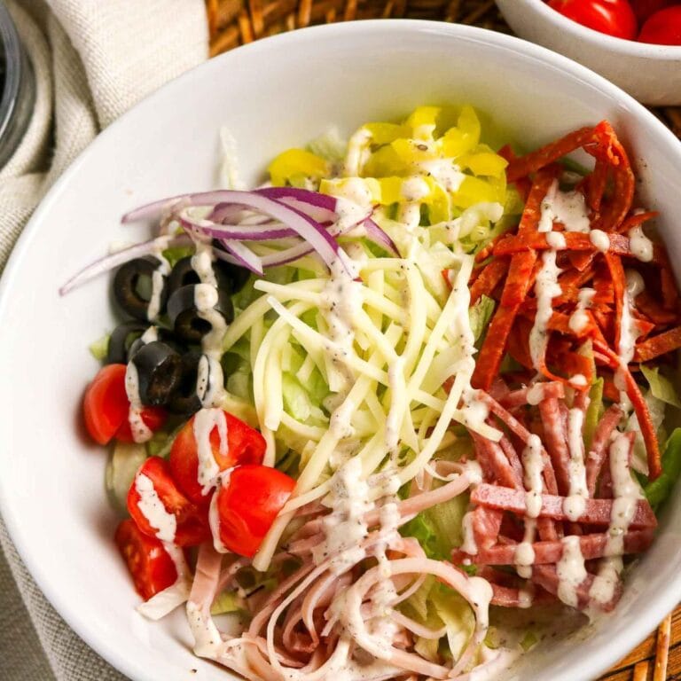 Closeup view of a white bowl filled with Italian Grinder Salad with deli meats, cheese, veggies and a creamy homemade dressing.