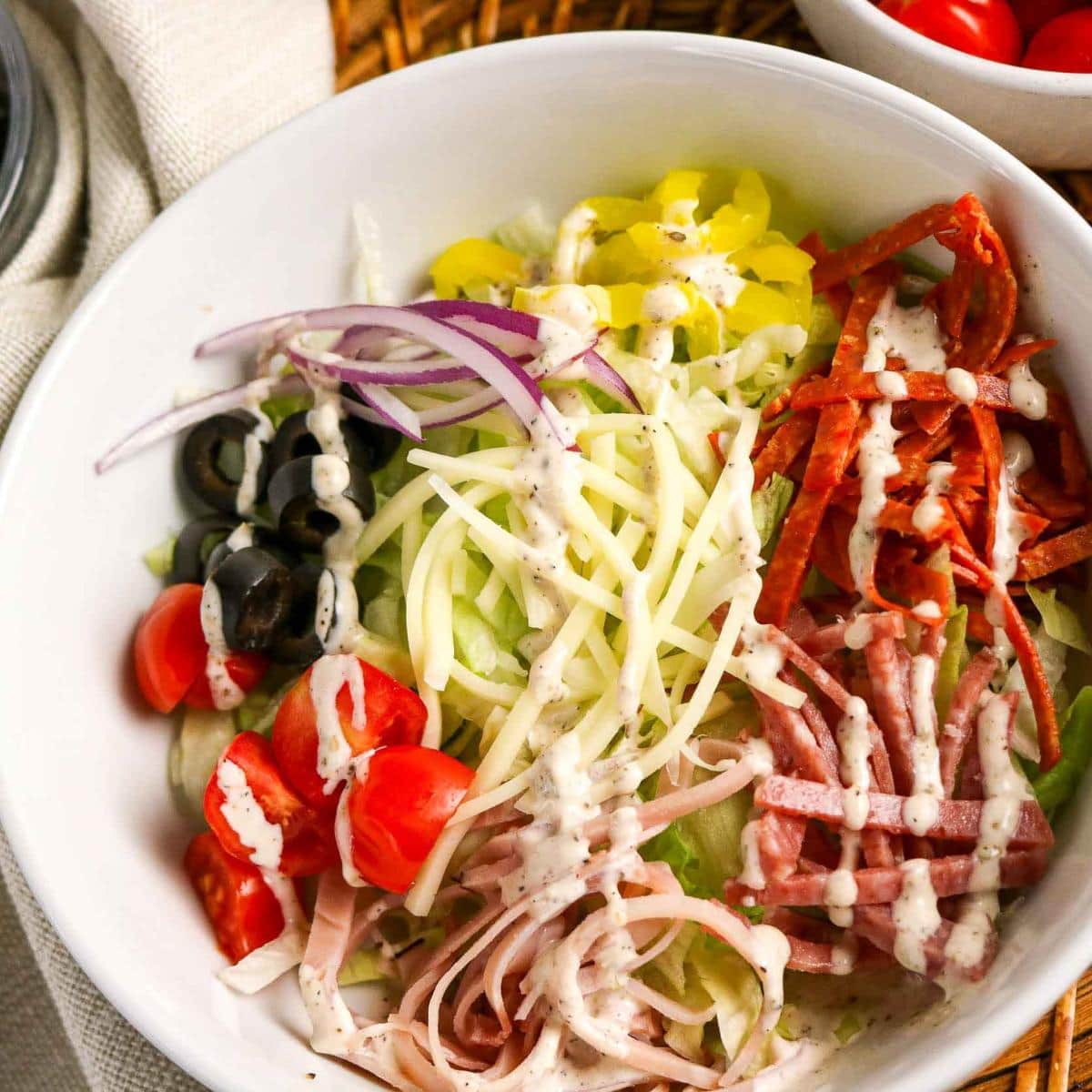 Closeup view of a white bowl filled with Italian Grinder Salad with deli meats, cheese, veggies and a creamy homemade dressing.