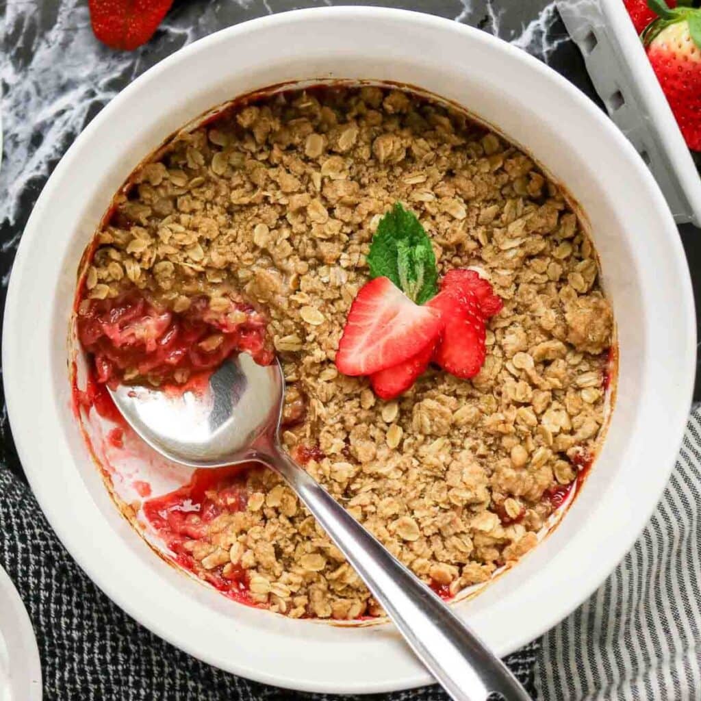 White bowl filled with strawberry crumble.