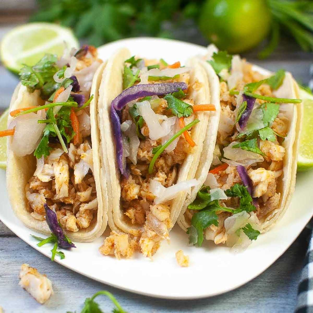 Air fryer tilapia fish tacos on a white plate garnished with cilantro lime slaw and lime wedges.