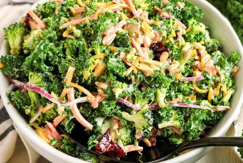 Close up view of kale and broccoli salad in a white bowl.