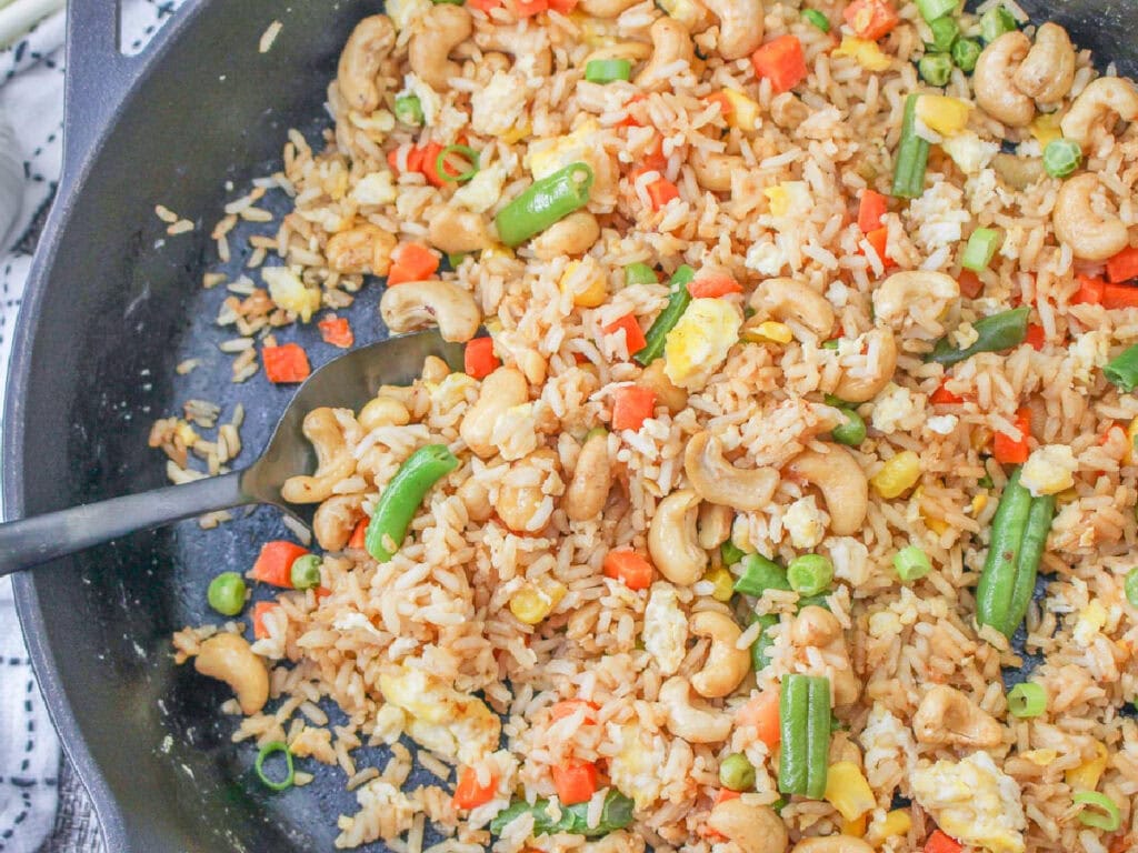 Cashew fried rice in a black skillet with a spoon.