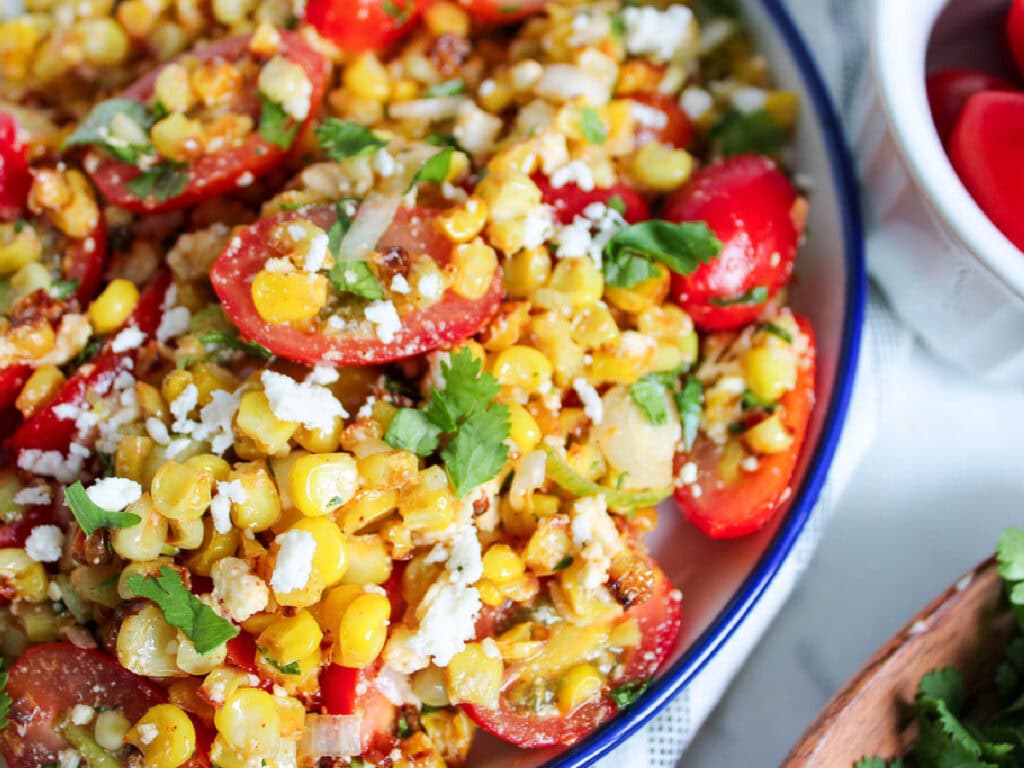 Close up of charred corn salad with fresh cilantro, tomato, queso cheese in a bowl
