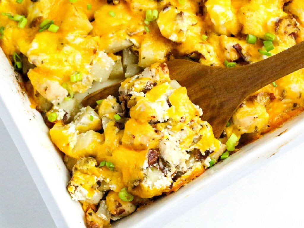 Scooping out the chicken bacon ranch potato bake from the casserole dish with a wooden spoon.