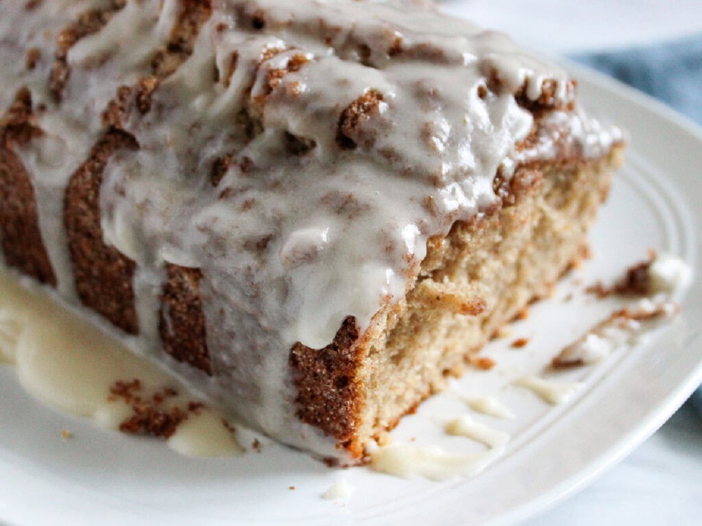 A cinnamon loaf topped with icing on a white serving plate.