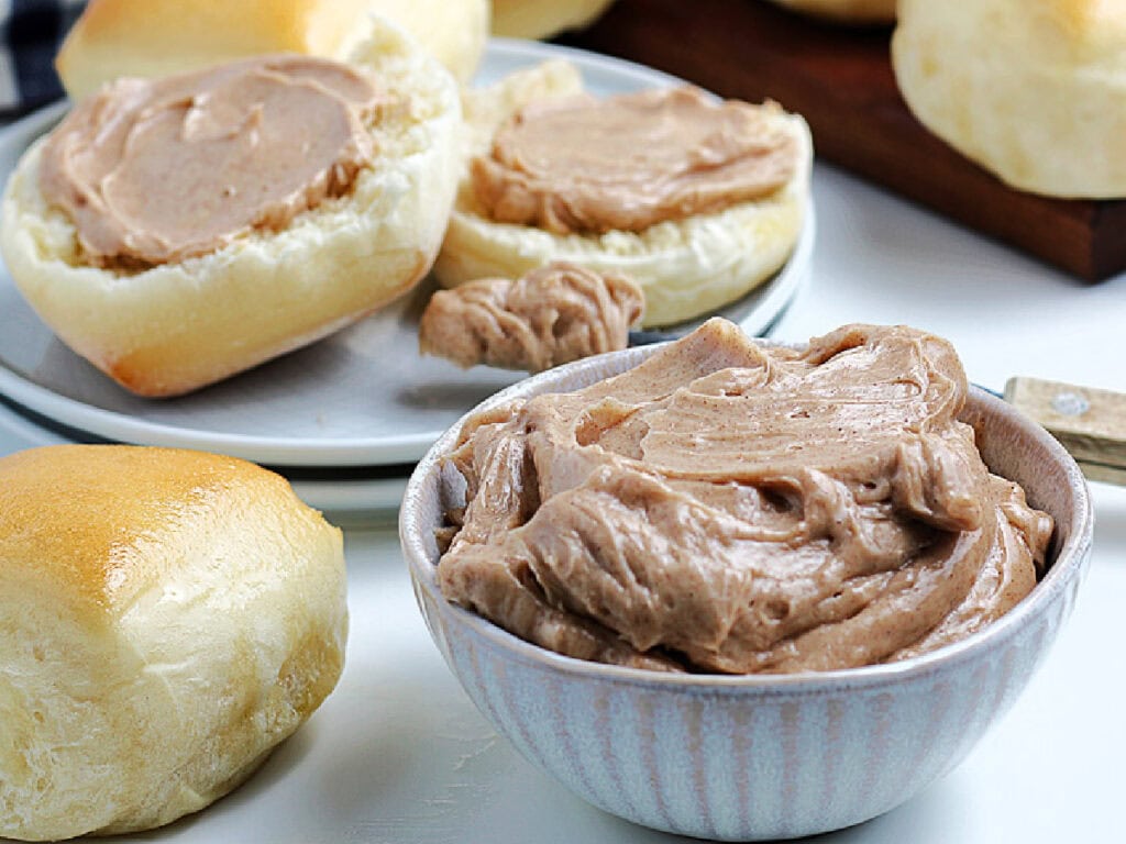 A small white ramekin of homemade Texas roadhouse cinnamon butter with yeast rolls in the background.