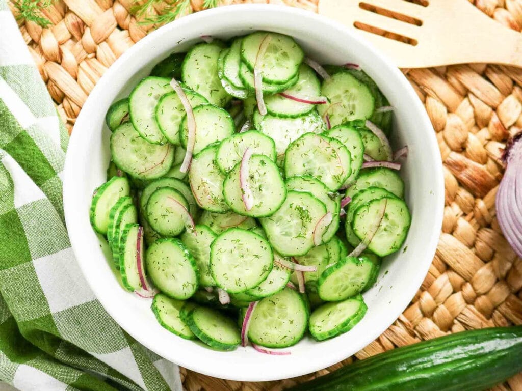 White bowl filled with sliced cucumber and dill salad.