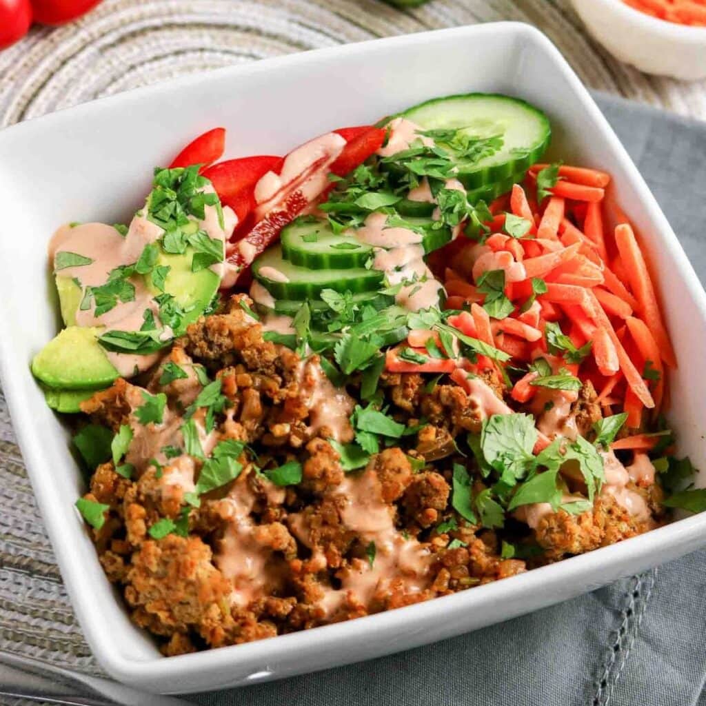 Ground turkey rice bowls with sliced cucumbers, carrots, avocado and spicy sauce on top.