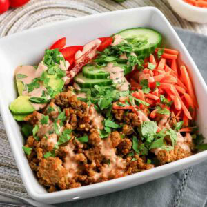 Ground turkey rice bowls with sliced cucumbers, carrots, avocado and spicy sauce on top.