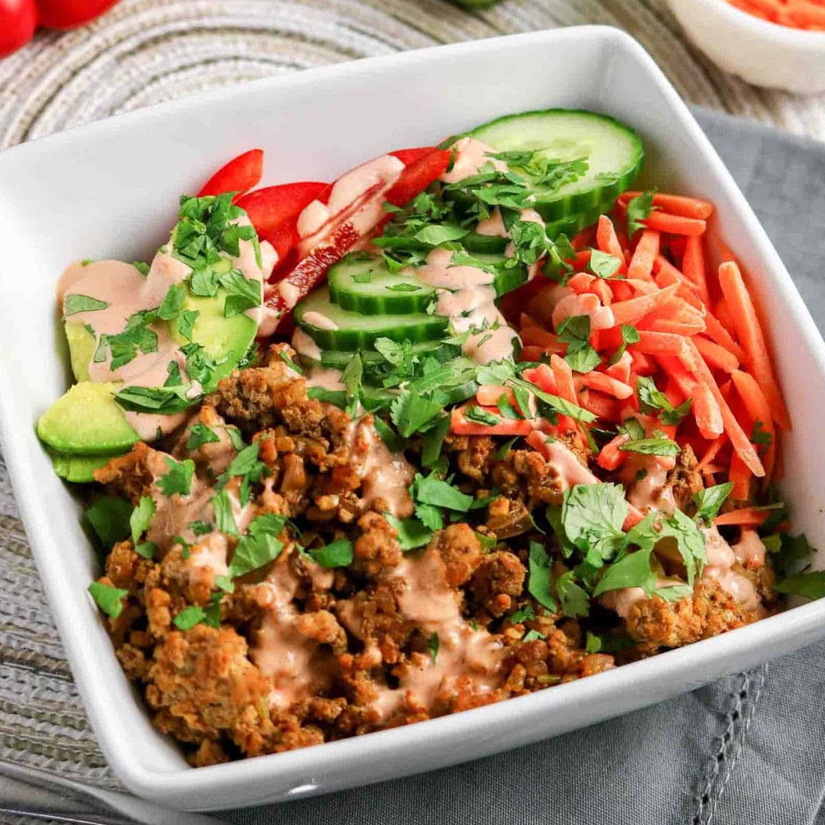 Ground turkey rice bowls with sliced cucumbers, carrots, avocado and spicy sauce on top.