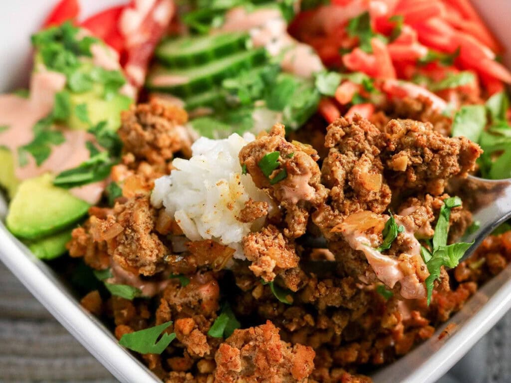 Close up view of a bite of ground turkey rice bowl on a fork with the bowl in the background.