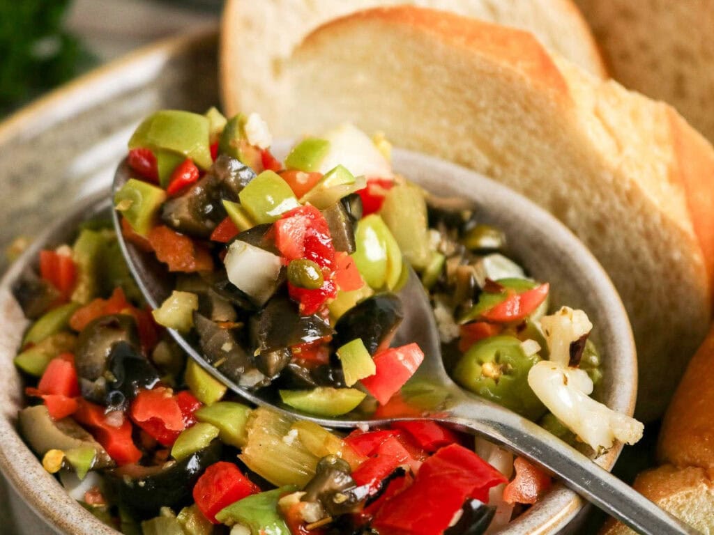 Close up view of chopped Muffaletta Olive Salad on a spoon with bread slices.