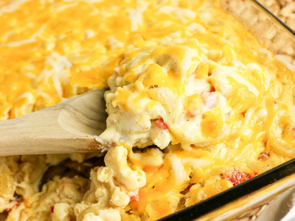 Wooden spoon scooping out a serving of mac and cheese with pimentos.