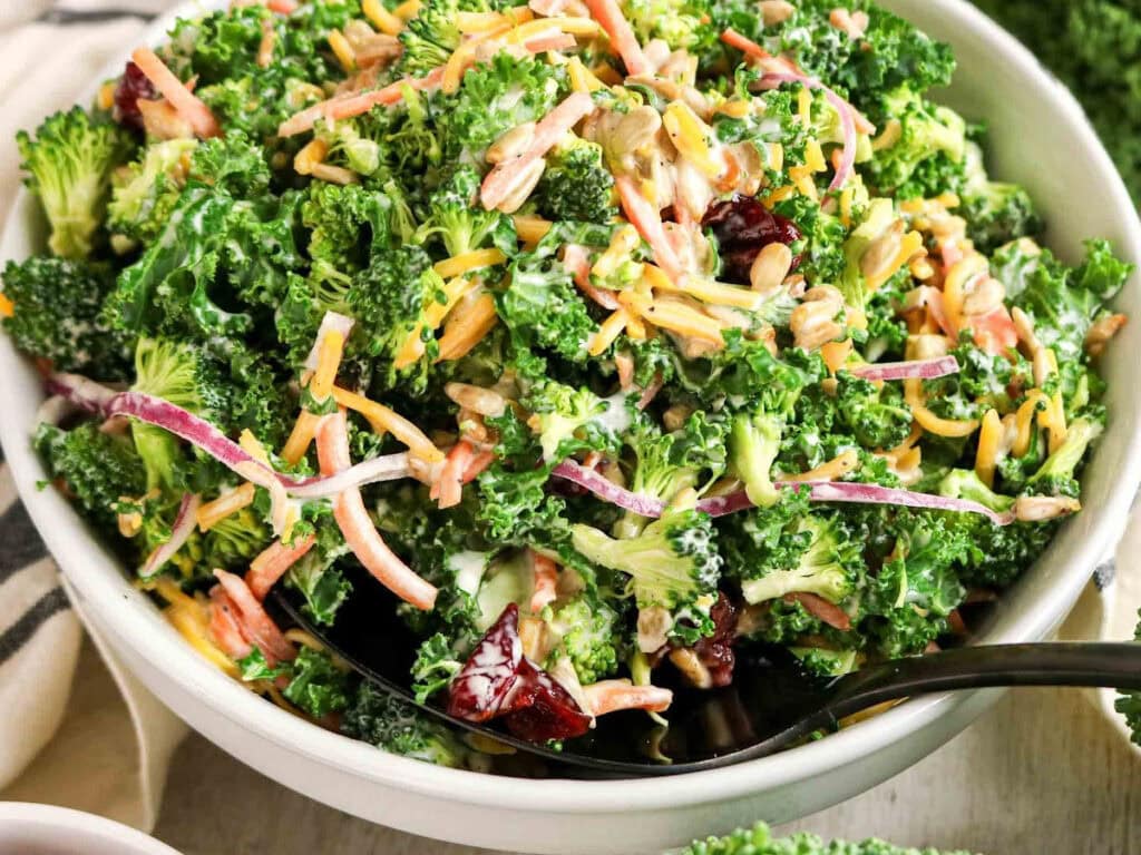 Close up view of kale and broccoli salad in a white bowl.