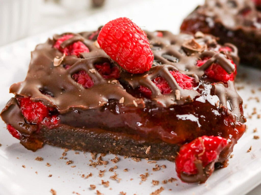 Raspberry chocolate squares on a white serving dish topped with fresh berries.