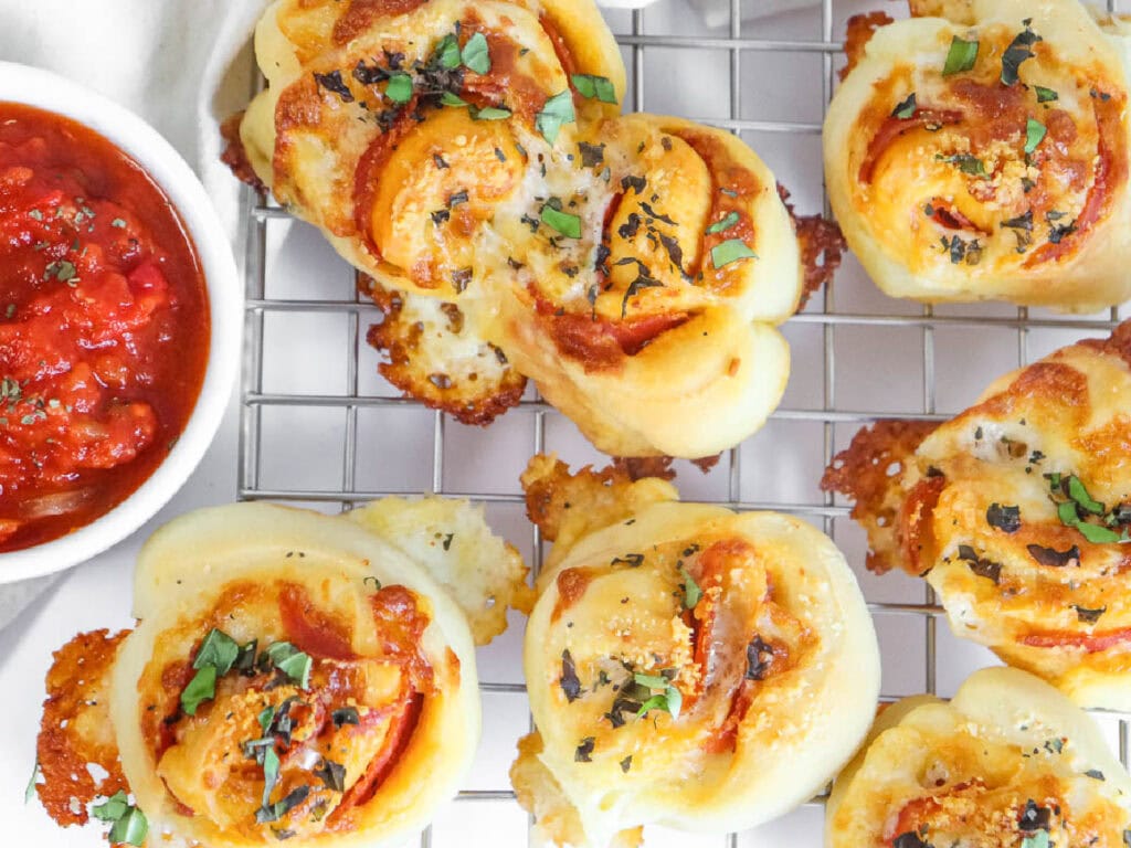 Top view of pepperoni rolls on a wire cooling rack with a bowl of marinara sauce.