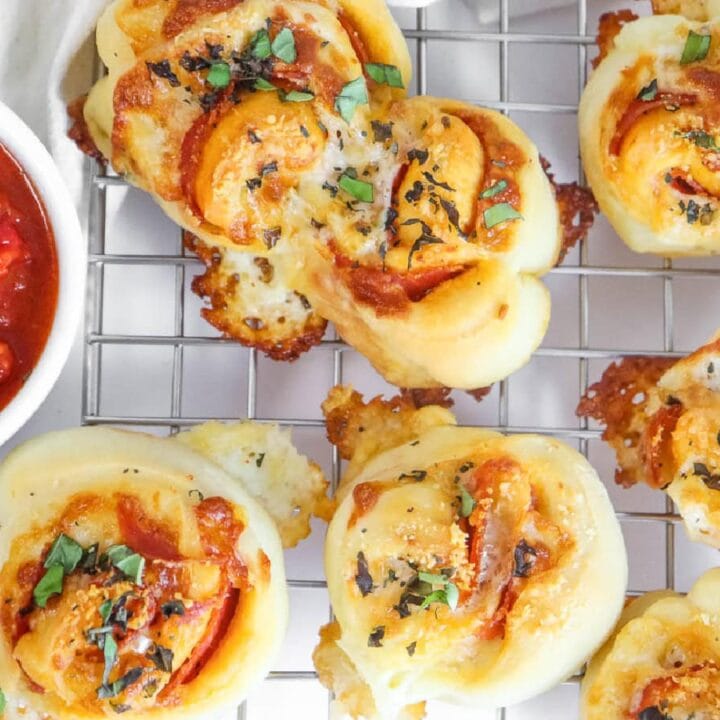 Top view of pepperoni rolls on a wire cooling rack with a bowl of marinara sauce.