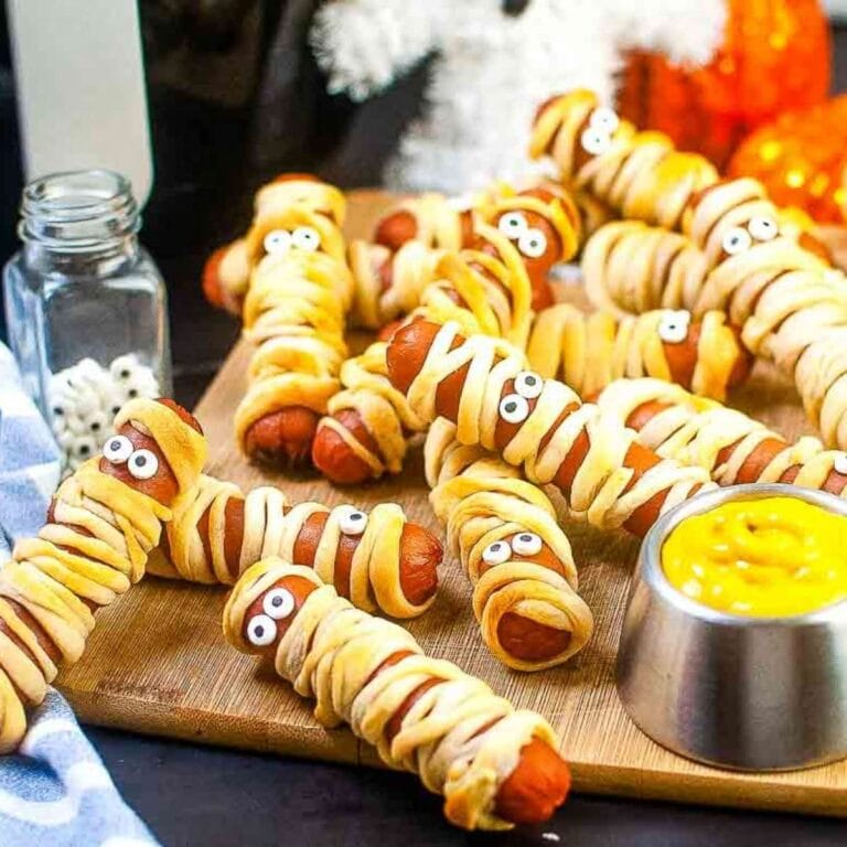 Closeup of air fryer mummy dogs on a wood cutting board with a ramekin of yellow mustard.