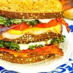 Air fryer turkey sandwich with bacon, cheese, lettuce and tomato on a white plate.