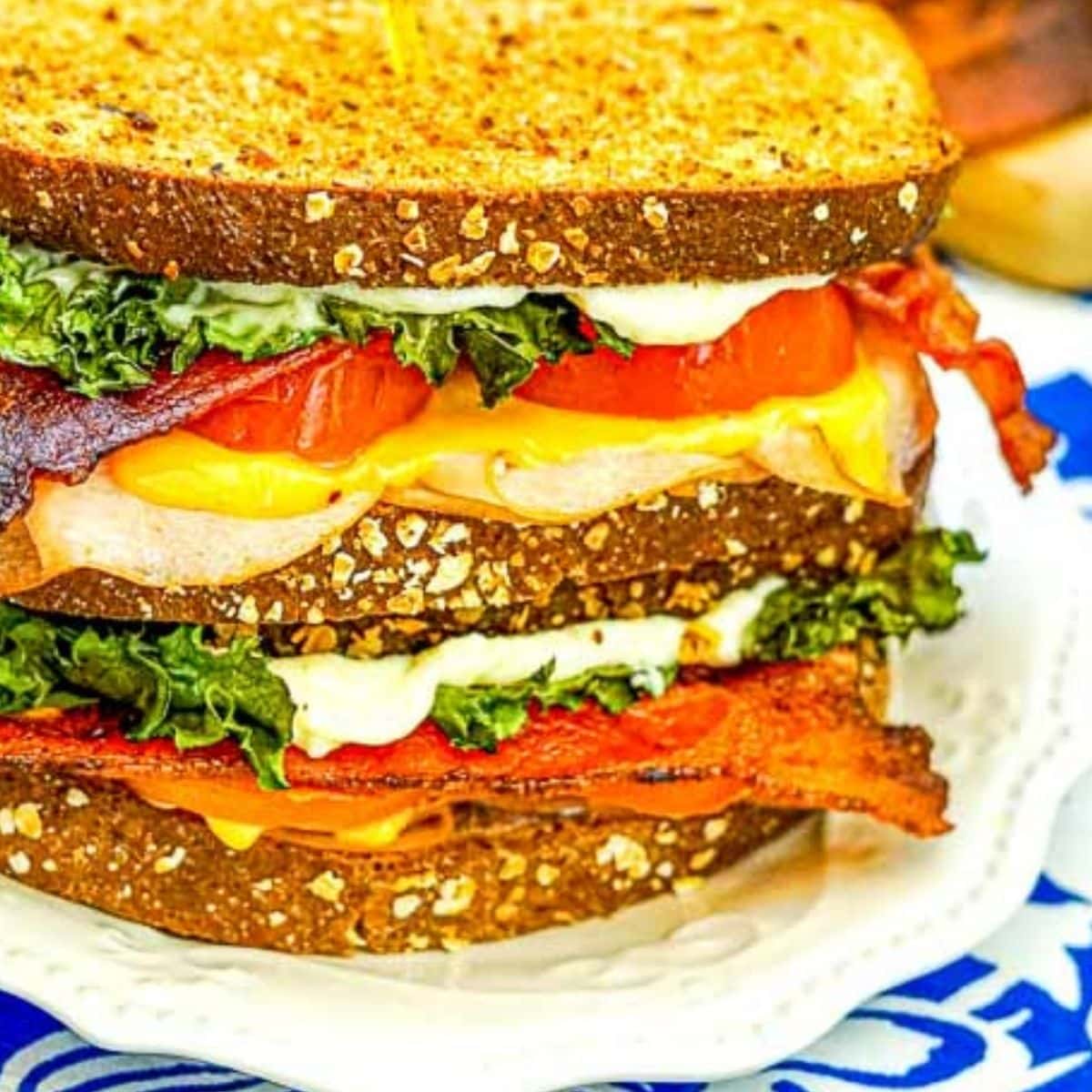 Air fryer turkey sandwich with bacon, cheese, lettuce and tomato on a white plate.