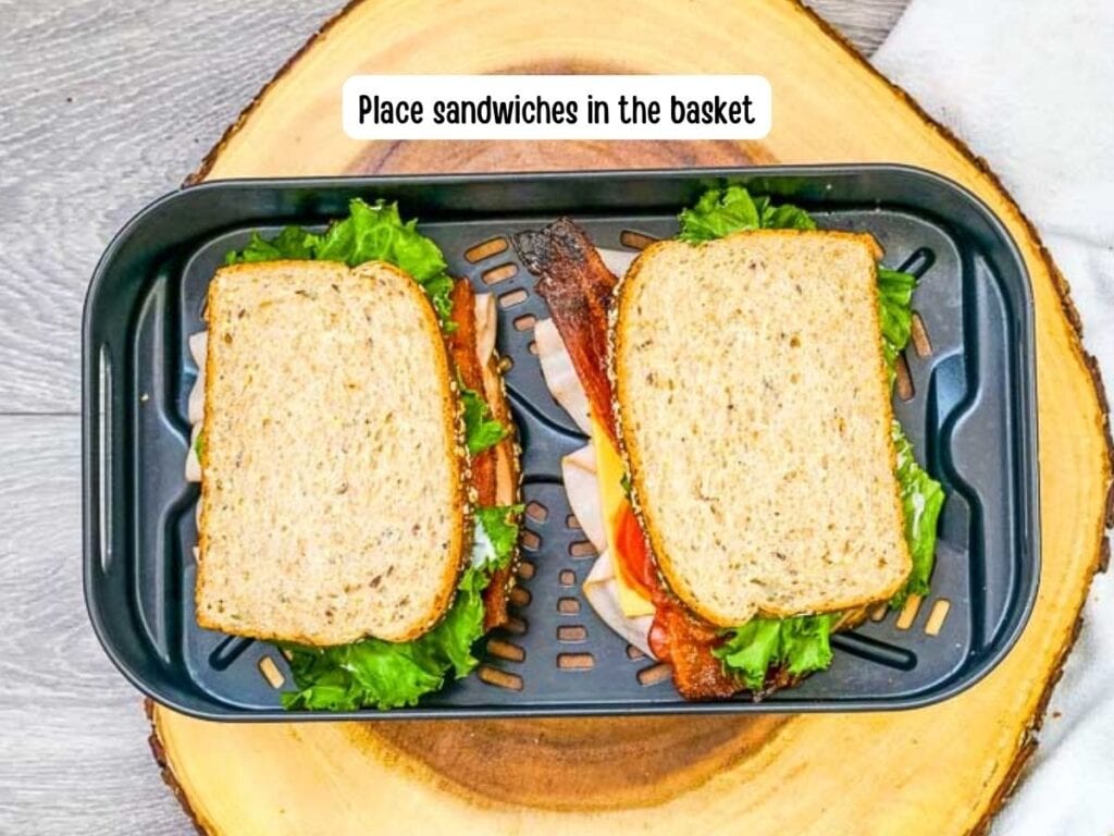 Two turkey club sandwiches placed in the air fryer basket.